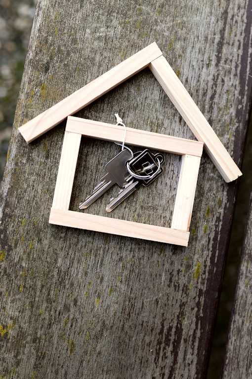 Claves para encontrar tu nuevo hogar en España Llaves con marco de casa de madera sobre una mesa, representando servicios de reubicación y búsqueda de vivienda en España.